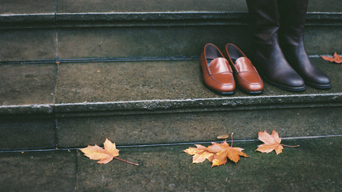 Brown leather loafers and dark leather boots resting on wet slate steps beside fallen maple leaves